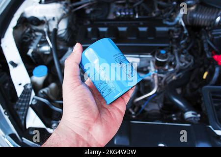 Le filtre à huile pour moteur d'automobile tient dans la main de mécanicien d'automobile avec un compartiment moteur de voiture sur le fond, concept d'entretien d'auto Banque D'Images