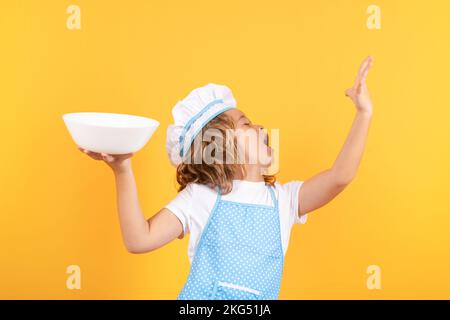 Drôle de chef cuisinier enfant avec plaque de cuisine, portrait de studio. Enfant en uniforme de cuisinière et chapeau de chef préparant des aliments sur fond de couleur studio. Cuisson Banque D'Images