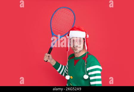 Joyeux Noël. joyeux homme en costume d'elfe et chapeau du père noël. noël gars tenir la fusée de tennis Banque D'Images