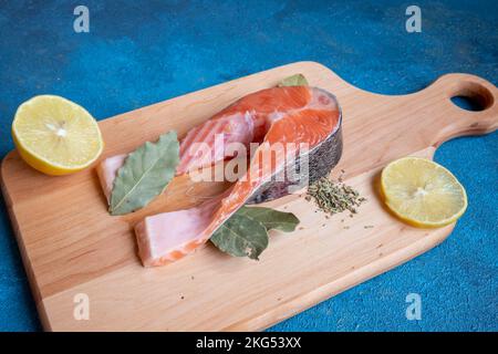 Un morceau de poisson se trouve sur une planche sur fond bleu. À proximité se trouve un demi citron et une feuille de baie. Banque D'Images