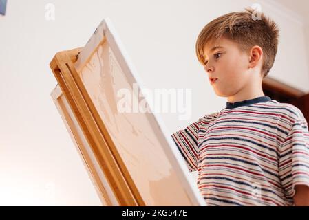 Un garçon peint une image sur toile avec un pinceau et des peintures. Banque D'Images