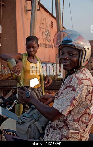 Jeune homme achetant de l'essence pour sa moto, Azove, Couffo, Bénin. De nombreux stands sont visibles le long de la route, vendant de petites quantités d'essence Banque D'Images