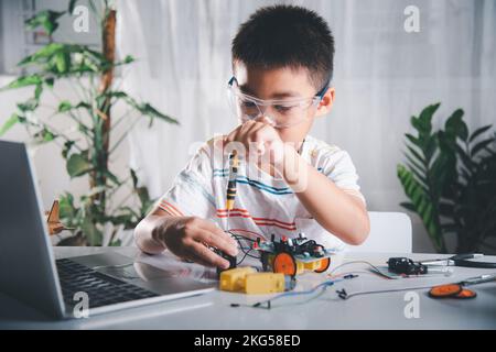 Enfant asiatique assemblant le projet de travail de robot de voiture Arduino à la maison Banque D'Images