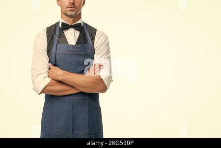 Homme plein de confiance vue de récolte dans l'arc et le tablier barman en gardant les bras croisés isolés sur blanc, espace de copie Banque D'Images