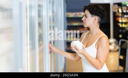 Une femme hispanique intéressée choisit des produits laitiers sur des étagères réfrigérées en magasin Banque D'Images