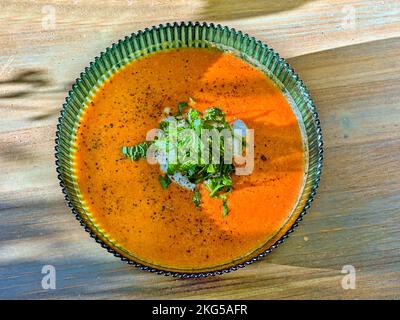 Vue de dessus d'un bol en verre vert avec potiron orange et soupe de carottes. Herbes vertes fraîchement hachées au milieu. Le bol est sur une table en bois. Banque D'Images