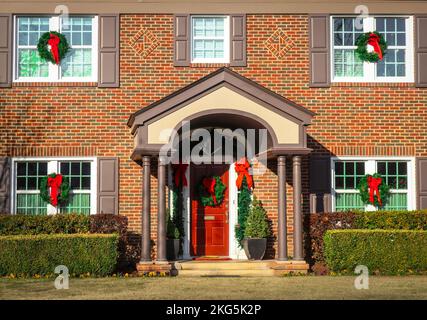 Entrée d'une maison en brique de deux étages avec porche voûté décoré pour Noël avec des couronnes sur les fenêtres et guirlande avec des rubans rouges Banque D'Images