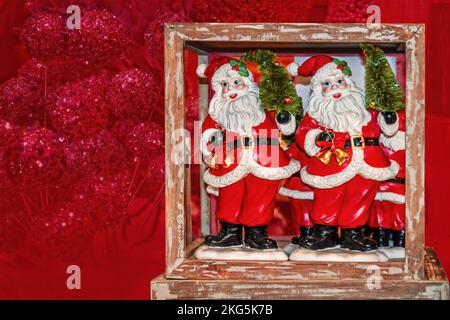 Santa Twins dans une boîte - décorations de Noël - figurines du Père Noël avec des cloches et des arbres dans une boîte rustique en bois sur fond rouge décoloré - Chambre pour Banque D'Images