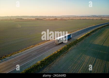 Vue aérienne d'un semi-camion à mouvement rapide et flou avec une remorque de chargement roulant sur autoroute transportant des marchandises en soirée. Transport et logistique de livraison Banque D'Images