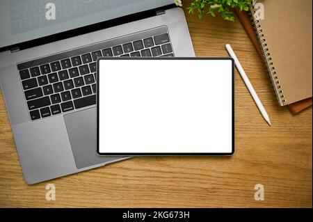 Vue de dessus, espace de travail minimal avec la tablette numérique écran blanc maquette pour l'affichage votre graphique est sur ordinateur portable, stylet et livre sur fond de bois. Banque D'Images