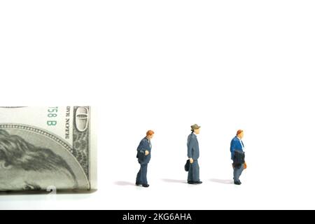 Photographie miniature de personnage de jouet de personnes. Concept d'indemnité de départ pour les travailleurs licenciés. Trois hommes d'affaires avec des dollars roués d'argent. Isolé sur bac blanc Banque D'Images