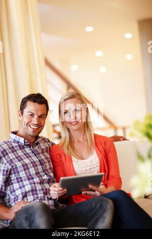 La technologie rend notre vie beaucoup plus facile. Un couple heureux assis sur leur canapé travaillant sur une tablette numérique - copyspace. Banque D'Images