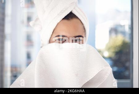 Portrait, serviette et femme après une douche, heureux et se détendre tout en cachant le visage et le toilettage dans sa maison. Timide, fille et beauté, soins de la peau et routine dans Banque D'Images