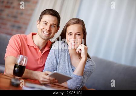 Album photo numérique à bord. Portrait d'un jeune couple souriant lorsqu'il utilise une tablette numérique à la maison. Banque D'Images