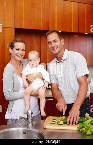 Super d'être à la maison. Un portrait d'un couple heureux tenant son bébé tout en étant debout dans la cuisine. Banque D'Images