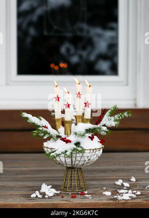 Couronne de l'Avent avec quatre bougies allumées blanches et des étoiles en bois rouge dans un panier en métal rempli de neige décoré de branches de sapin. Décoration de jardin pour Banque D'Images