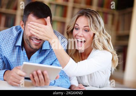Vous ne pouvez pas le voir. un jeune couple choqué assis à la maison à l'aide d'une tablette numérique. Banque D'Images