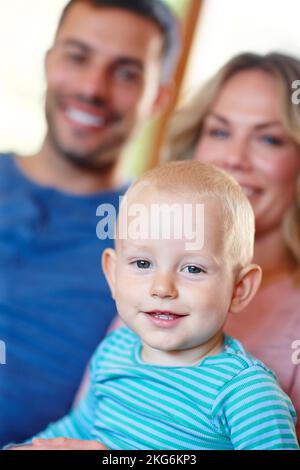 HES le petit gars le plus mignon... Portrait d'une jeune famille heureuse assise à la maison. Banque D'Images