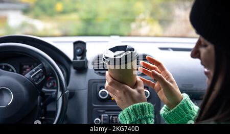 Une jeune femme avec une tasse de café s'assoit dans la voiture, concept de voyage. Banque D'Images