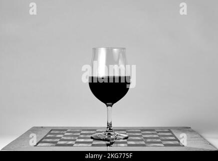 Verre à vin rouge debout sur l'échiquier. Macro gros plan sur fond blanc. Photo noir et blanc. Verres à vin. Jeu d'échecs. Banque D'Images