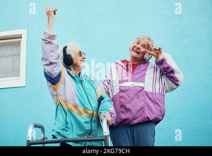 Senior, musique et handicap avec une femme amis en plein air dans une ville s'amusant avec un geste de main signe de paix. Liberté, retraite et heureux Banque D'Images