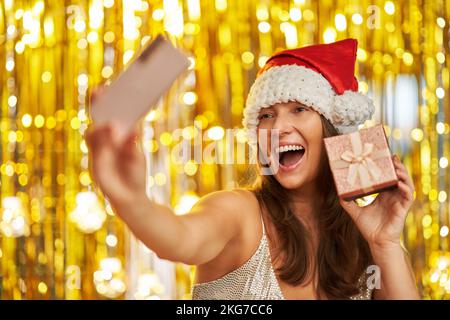 Femme sur fond d'or dans le chapeau du Père Noël avec téléphone Banque D'Images