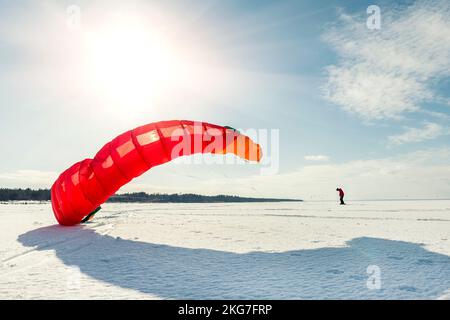 Vue panoramique de beaucoup de gens amis aiment faire du kite surf planche en costume chaud lors de la journée d'hiver ensoleillée et lumineuse à la surface enneigée du lac gelé Banque D'Images