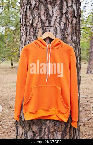 pull à capuche orange accroché à un cintre sur un arbre dans la forêt. Démonstration de différentes couleurs de vêtements Banque D'Images