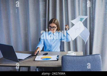 Une femme responsable est folle à son bureau et jette des documents. Une journée de travail dure au bureau. Travailleur émotionnel. Banque D'Images