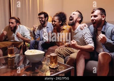 Fans de football multiracial regardant un match de football à la télévision et célébrant la victoire Banque D'Images