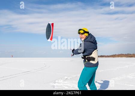 Vue panoramique de beaucoup de gens amis aiment faire du kite surf planche en costume chaud lors de la journée d'hiver ensoleillée et lumineuse à la surface enneigée du lac gelé Banque D'Images