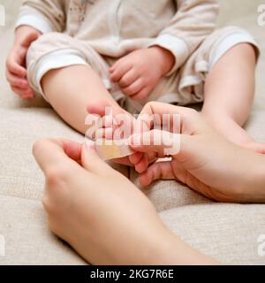 Mère femme colle un bracelet médical sur la jambe du bébé. Main de maman avec ruban adhésif de protection collant et pied d'enfant. Enfant âgé d'un an et t Banque D'Images