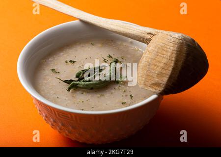 Soupe traditionnelle marocaine à la crème d'orge ou belboula avec une cuillère en bois sur fond orange Banque D'Images