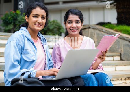 Concentrez-vous sur la jeune fille avec un livre, les étudiants heureux de l'université regardant la caméra tout en travaillant sur un ordinateur portable sur le campus universitaire - concept de l'éducation, le travail d'équipe Banque D'Images