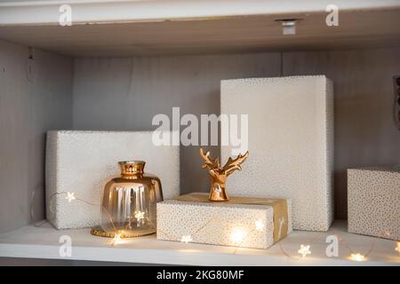 Derrière le verre d'une armoire avec vaisselle, les étagères sont décorées de jouets de Noël, guirlandes lumineuses, cadeaux dans un emballage rose. Jouets en forme de Banque D'Images