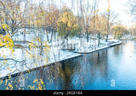 Paysage d'hiver. Parc municipal avec rivière, bancs et arbres couverts de neige, personnes marchant, à Riga, Lettonie Banque D'Images