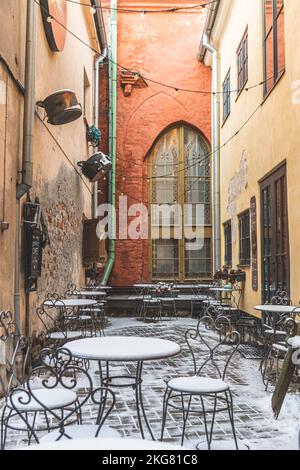 Entrée avec panneau d'un café confortable dans la vieille ville de Riga, Lettonie, en hiver avec des tables et des chaises couvertes de neige et de lumière vintage, verticale Banque D'Images