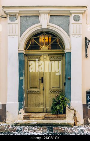 Ancienne porte en bois d'époque d'un bâtiment majestueux dans la vieille ville de Riga avec un véritable petit arbre de Noël sur la marche en hiver, vertical Banque D'Images