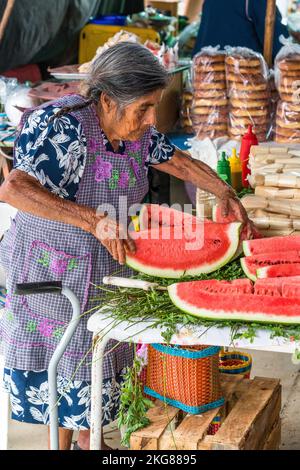 Une femme Zapotec âgée en robe typique prépare la pastèque à la vente sur le marché hebdomadaire de Zaachila, Oaxaca, Mexique. Banque D'Images