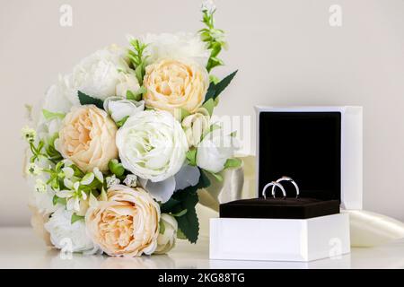 Une paire d'anneaux de mariage brillants affichés dans une boîte en anneau en plus du bouquet traditionnel de fleurs de mariage, roses blanches et de pêche. Symbole de l'amour, r Banque D'Images