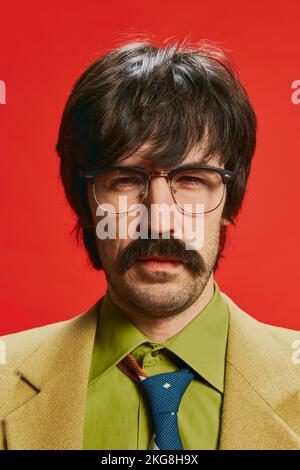 Portrait en gros plan d'un homme élégant avec moustache posé dans un costume vintage isolé sur fond rouge. Aspect suspect Banque D'Images