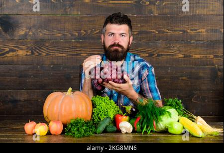 Concept d'agriculture et de récolte. L'homme barbu tient le fond en bois de raisin. Agriculteur avec récolte locale sur table. Récolte biologique de légumes. Agriculteur Banque D'Images