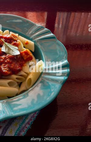 Goias, Brésil – 22 novembre 2022 : détail d'une assiette verte avec une portion de pâtes (penne), sauce tomate et feuilles de basilic. Banque D'Images