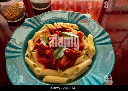 Goias, Brésil – 22 novembre 2022 : une assiette verte avec une portion de pâtes (penne), sauce tomate et feuilles de basilic. Banque D'Images