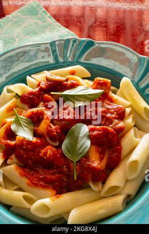 Goias, Brésil – 22 novembre 2022 : détail d'une assiette verte avec une portion de pâtes (penne), sauce tomate et feuilles de basilic. Banque D'Images