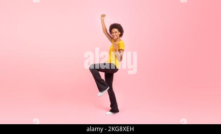 Heureuse femme maurique afro-américaine du millénaire étudiante dans les réjouissances décontractées, fait le geste de la victoire et du succès Banque D'Images