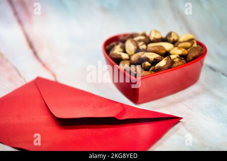 Noix du Brésil dans un plat en forme de coeur avec carte d'enveloppe. Cadeau de Saint-Valentin pour quelqu'un. Banque D'Images