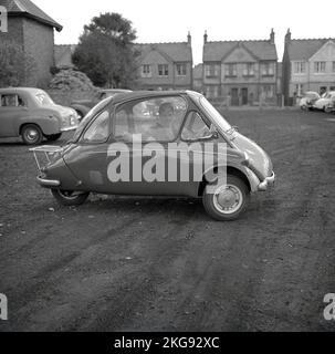 1960s, historique, à l'extérieur dans un parking en gravier, un homme assis à l'intérieur d'une petite voiture de l'époque, une voiture à bulles, une BMW Isetta, qui avait une porte d'ouverture avant, Wycombe, Angleterre, Royaume-Uni. Construite pour la première fois par ISO spa en Italie en 1953, cette petite voiture a été construite sous licence dans différents pays, y compris par BMW en Allemagne jusqu'en 1962 et connue sous le nom de « Bubble car ». Banque D'Images