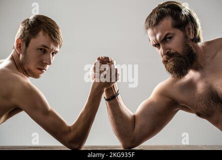 Lutte de bras. Homme barbu fortement musclé bras luttant un homme faible et puny. Bras luttant main mince, gros bras fort en studio. Deux mains d'homme ont classé Banque D'Images