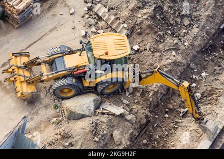 Tracteur jaune avec godet et arrière et avant, creusant une tranchée sur un chantier de construction. Vue de dessus Banque D'Images